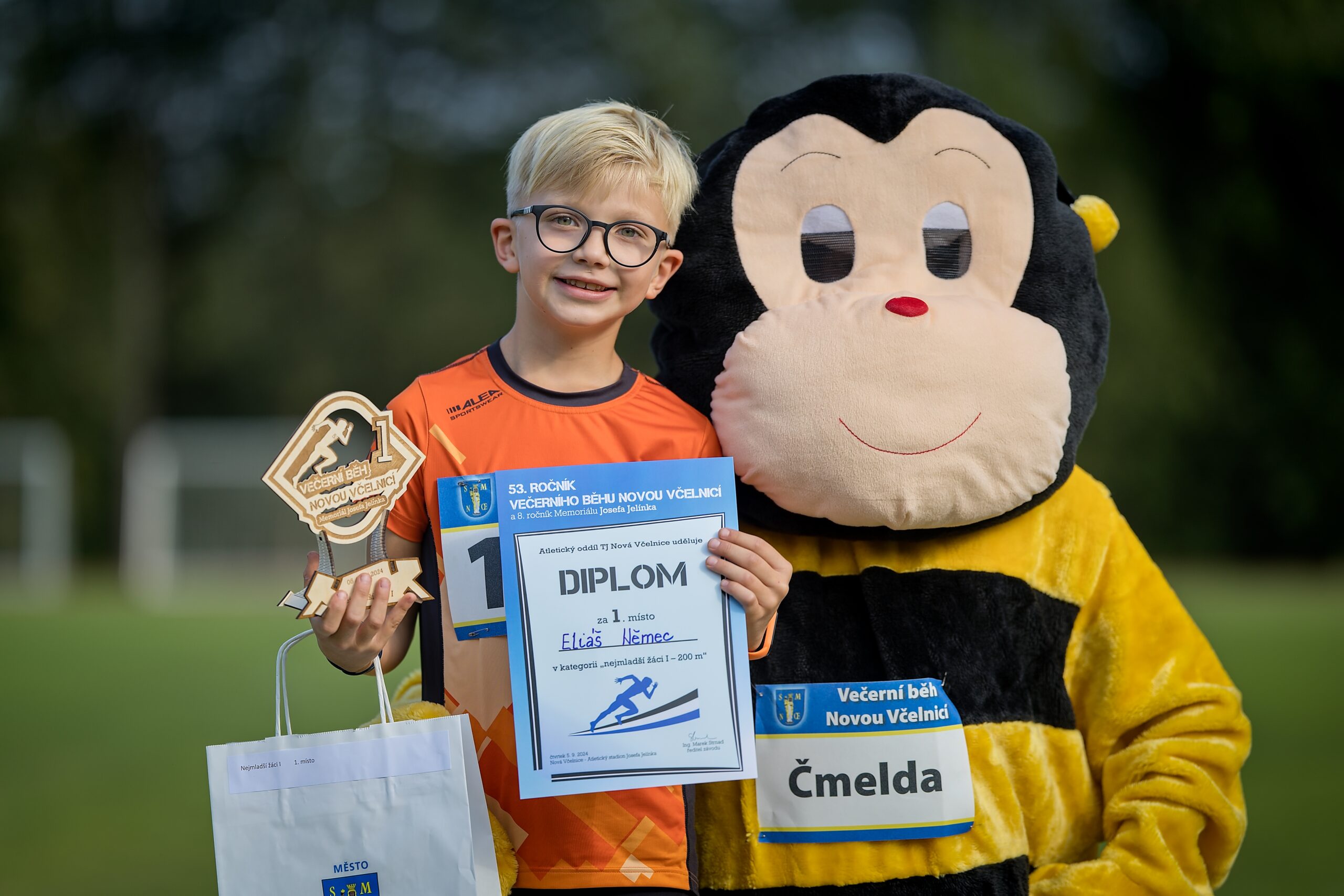 dítě držící dřevěnou trofej, stojící maskot závodu