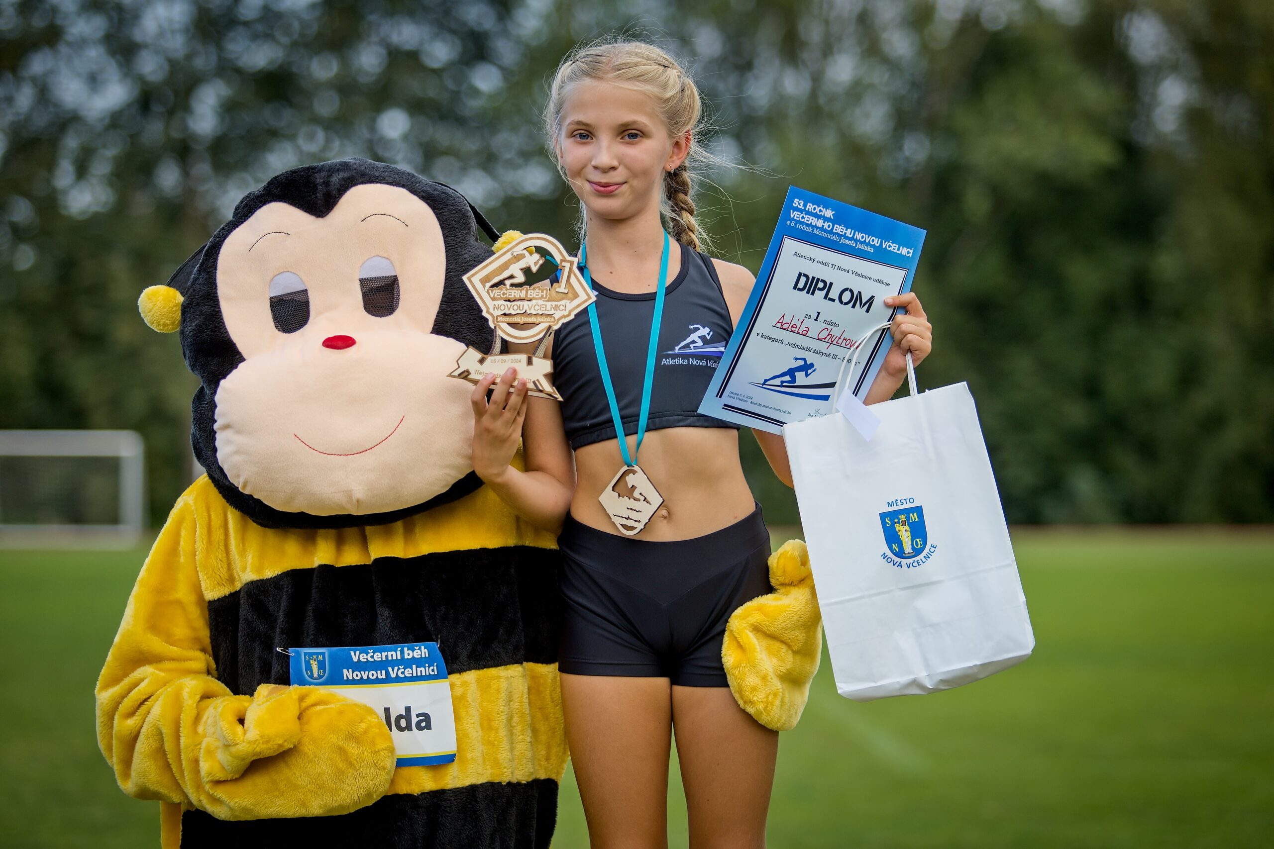 dítě držící dřevěnou trofej, stojící maskot závodu